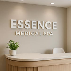 May include: A white sign with the text "ESSENCE MEDICAL SPA" on a beige wall. A wooden reception desk with a white countertop is in the foreground.