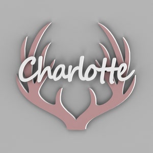 May include: A decorative wall hanging featuring the name "Charlotte" in white script, set against a pink antler design with a white outline. The antlers are a soft pink color, creating a layered effect against a gray background.