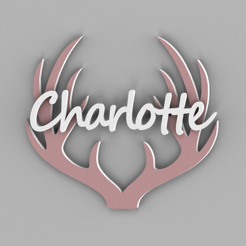 May include: A decorative wall hanging featuring the name "Charlotte" in white script, set against a pink antler design with a white outline. The antlers are a soft pink color, creating a layered effect against a gray background.