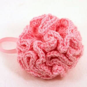 May include: A pink crocheted bath puff with a ruffled texture. The puff is tied with a pink ribbon.