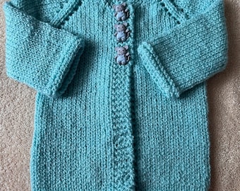 May include: A hand-knitted turquoise cardigan featuring long sleeves, a ribbed texture, and three decorative buttons shaped like small gray mice wearing blue overalls. The garment has a V-neckline and a vertical ribbed placket down the center.