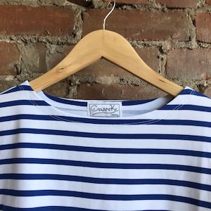 May include: A white and blue striped t-shirt with a navy blue collar and a "Crank Clothing" label.