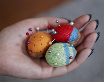 Può includere: Quattro spilli da cucito colorati a forma di palla, ognuno con una varietà di spilli di diversi colori inseriti. Gli spilli da cucito sono fatti di diversi tessuti, tra cui rosso, blu, verde e arancione.