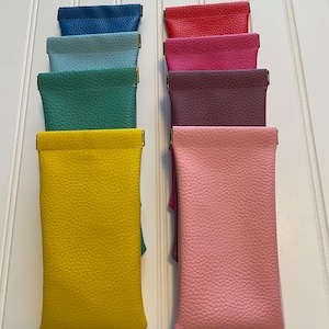 May include: A collection of eight rectangular pouches with a textured surface, arranged in two vertical columns. The pouches feature a variety of solid colors including blue, light blue, teal, yellow, red, magenta, dark purple, and light pink.