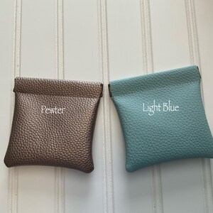 May include: Two small, square pouches in a top-down view. One is pewter-colored with the word "Pewter" embroidered on it. The other is light blue with "Light Blue" embroidered on it. Both pouches have a textured surface.