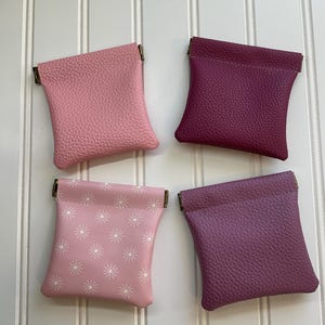 May include: Four small, leather coin purses in shades of pink and purple. Two purses are solid colors, while the other two feature a white starburst pattern. Each purse has a metal clasp.