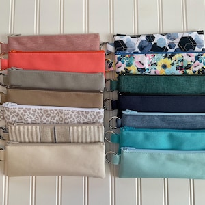 May include: A collection of fourteen rectangular zipper pouches arranged in two columns. The pouches feature various solid colors, including coral, gray, tan, beige, teal, and light blue, alongside patterns like leopard print, stripes, and florals.