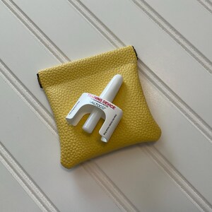 May include: A white training device with the text "TRAINING DEVICE ALTOCO" rests on a yellow textured pouch. The pouch is square-shaped with a black trim.