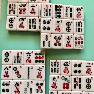 May include: A set of white mahjong tiles with red and black characters and symbols. The tiles are arranged in a grid pattern on a green surface. The tiles include numbers, winds, and dragons.