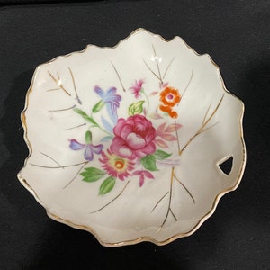 Könnte beinhalten: Eine weiße, blattförmige Schale aus Porzellan mit goldfarbenem Rand und Blumenmuster. Die Blumen sind rosa, orange, gelb, blau und grün.