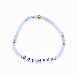 May include: A light blue beaded bracelet with gold accents and white letter beads spelling "BOY NANA".