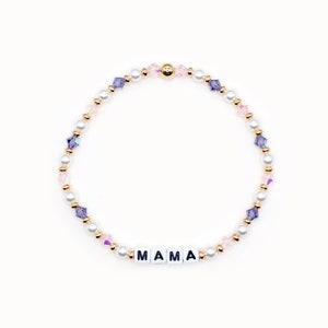 May include: A delicate bracelet featuring white pearls, gold beads, and purple and pink crystals. The bracelet spells out the word "MAMA" in white letters.