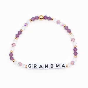 May include: A purple and clear crystal beaded bracelet with a gold clasp and the word "GRANDMA" spelled out in white beads.
