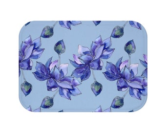 May include: A rectangular bath mat featuring a repeating pattern of watercolor-style blue lotus flowers and buds on a light blue background. The flowers have purple and white accents.