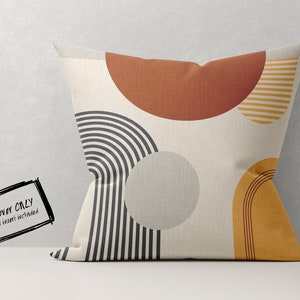 May include: A square decorative pillow cover with an abstract design. The pillow features geometric shapes in rust, mustard yellow, gray, and black on a cream background. The text "COVER ONLY NO insert included" is in the lower left corner.