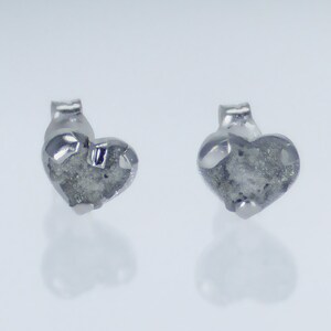 May include: A pair of silver heart-shaped earrings with a rough, textured surface.