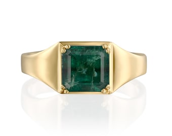 May include: A gold ring featuring a large, square-cut emerald gemstone. The ring has a classic signet style with a smooth, polished band and decorative accents near the emerald. The emerald is a deep, rich green color.