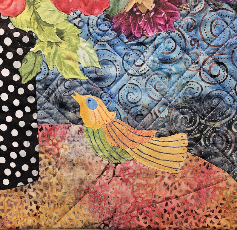 Puede incluir: Una colcha de retazos colorida con una aplicaci&oacute;n de p&aacute;jaro. El p&aacute;jaro es amarillo, verde y naranja con un ojo azul. La colcha est&aacute; hecha de varias telas con un patr&oacute;n de remolino azul y blanco, un patr&oacute;n de lunares negros y blancos y un patr&oacute;n floral marr&oacute;n y naranja.