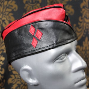 May include: A black leather hat with a red leather band and a red diamond pattern. The hat is worn on a mannequin's head.