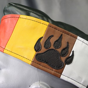 May include: A green leather hat with a multi-colored band. The band is red, yellow, brown, white, and gray. A black bear paw print is embroidered on the brown section of the band.