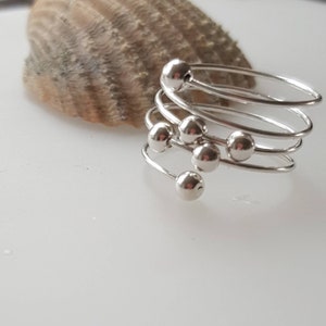 May include: A silver ring with multiple bands and round beads. The ring is coiled and the beads are arranged in a cluster.