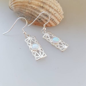 May include: A pair of silver earrings with a Celtic knot design and a white opal stone in each earring.
