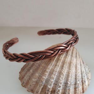 May include: A copper braided bangle bracelet. The bracelet is made of woven copper wire and has a simple, elegant design.