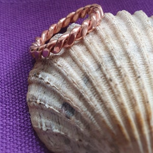 Pode incluir: Um anel de fio torcido em ouro rosa sobre um fundo de concha branca.