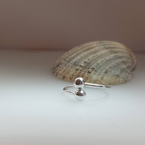 May include: A silver ring with two round balls on the top. The ring is open and can be adjusted to fit different finger sizes.