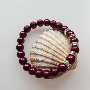 Puede incluir: Un brazalete de cuentas color burdeos con detalles plateados. El brazalete está hecho de cuentas redondas y tiene una fila de cuentas plateadas con diamantes de imitación.