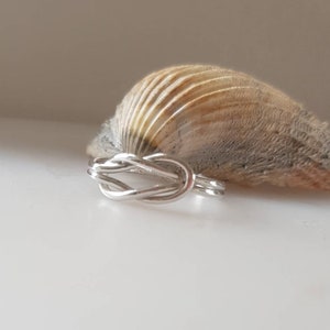 May include: A silver knot ring with a simple design. The ring is made of twisted wire and has a smooth finish.
