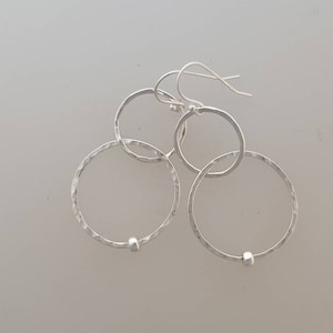 May include: Silver dangle earrings with two hammered circles connected by a small bead. The circles are slightly uneven in size.