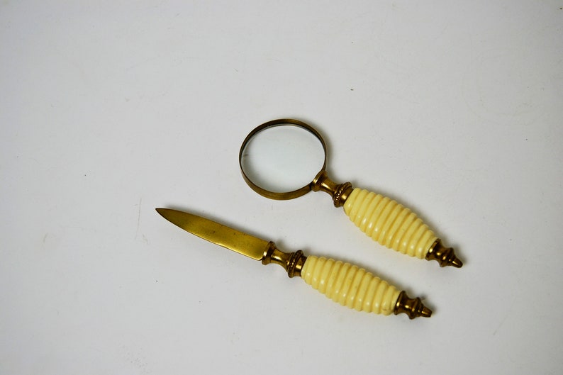 May include: A set of two brass desk accessories with ivory handles. The set includes a magnifying glass and a letter opener.