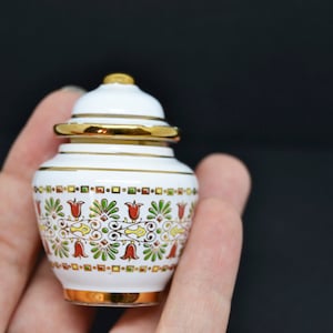 May include: A small white ceramic jar with a gold lid and intricate floral designs in red, green and yellow.