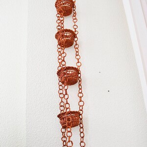 May include: A set of five brown woven hanging planters with a chain link design. The planters are suspended from the ceiling.