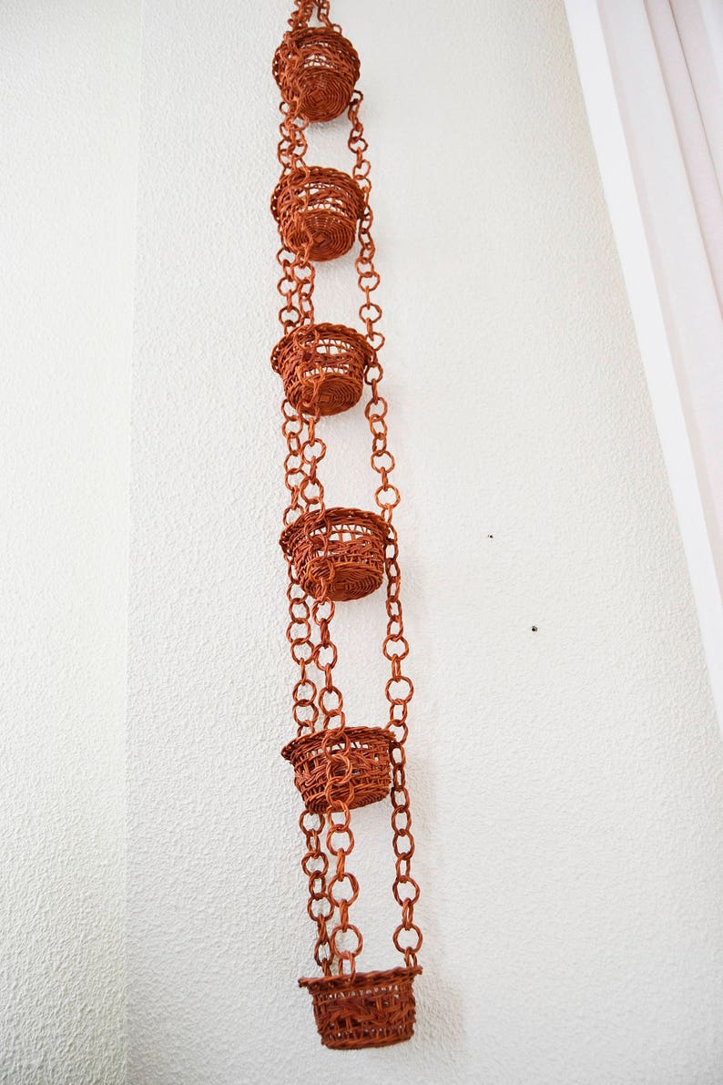May include: A set of five brown woven hanging planters with a chain link design. The planters are suspended from the ceiling.