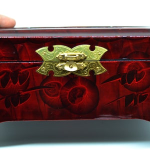 Peut inclure: Une bo&icirc;te en bois laqu&eacute; rouge avec un motif floral d&eacute;coratif. La bo&icirc;te est dot&eacute;e d'un fermoir et de charni&egrave;res dor&eacute;s. La surface a une finition brillante et le motif est de couleur rouge fonc&eacute;.