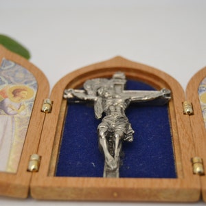 May include: A small wooden triptych with a silver crucifix inside. The triptych is open and the crucifix is visible. The triptych has two panels with images of angels on each side.