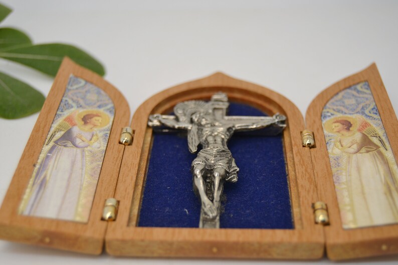 May include: A small wooden triptych with a silver crucifix inside. The triptych is open and the crucifix is visible. The triptych has two panels with images of angels on each side.