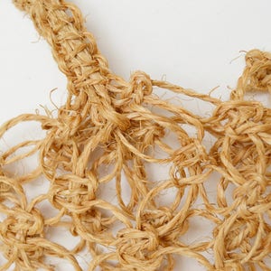 May include: Close-up of a natural fiber rope woven into a intricate knot pattern. The rope is a light brown color and the knots create a delicate, airy texture.