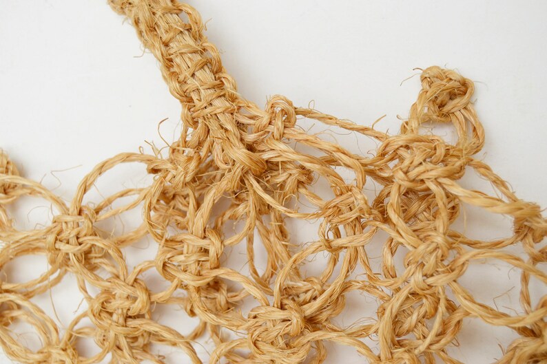 May include: Close-up of a natural fiber rope woven into a intricate knot pattern. The rope is a light brown color and the knots create a delicate, airy texture.