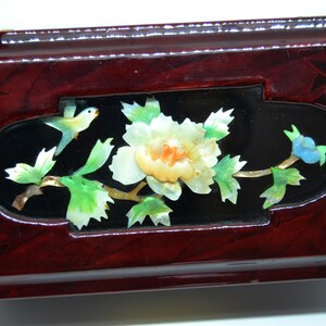 Peut inclure: Bo&icirc;te rectangulaire en bois laqu&eacute;, finition rouge fonc&eacute;. Le couvercle pr&eacute;sente une incrustation noire avec un motif floral et d'oiseaux en nacre. Le motif comprend une fleur blanche, des feuilles vertes et un oiseau bleu.