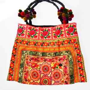 May include: A colorful embroidered tote bag with a black handle and pom-poms. The bag features a floral design with red, pink, yellow, and green colors.