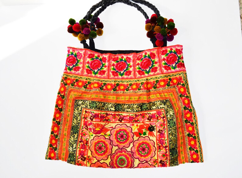 May include: A colorful embroidered tote bag with a black handle and pom-poms. The bag features a floral design with red, pink, yellow, and green colors.
