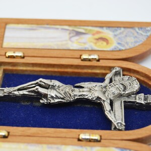 May include: A wooden triptych with a silver-toned crucifix inside. The triptych is closed, and the crucifix is visible through the open center panel. The other panels have images of religious figures.