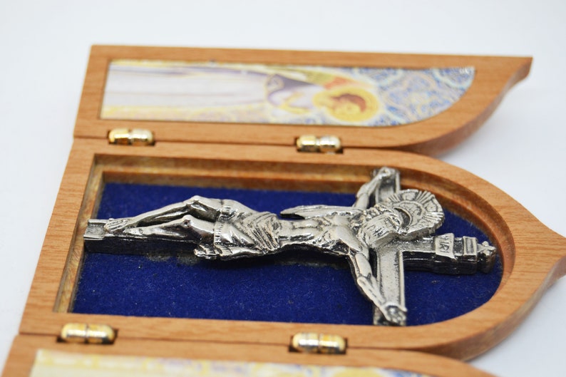 May include: A wooden triptych with a silver-toned crucifix inside. The triptych is closed, and the crucifix is visible through the open center panel. The other panels have images of religious figures.