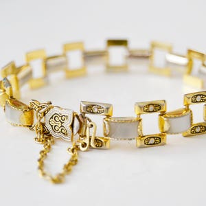 May include: A gold and white bracelet with a decorative clasp. The bracelet is made of linked squares with white enamel and gold accents.
