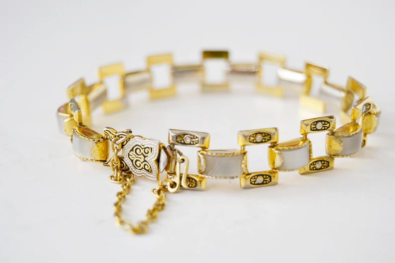 May include: A gold and white bracelet with a decorative clasp. The bracelet is made of linked squares with white enamel and gold accents.