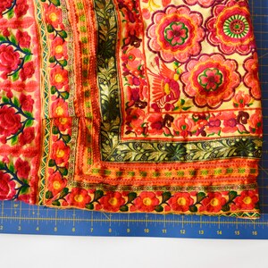 May include: A close-up of a colorful fabric with intricate embroidery featuring floral patterns and a bird design. The fabric is a mix of red, orange, yellow, green, and black.