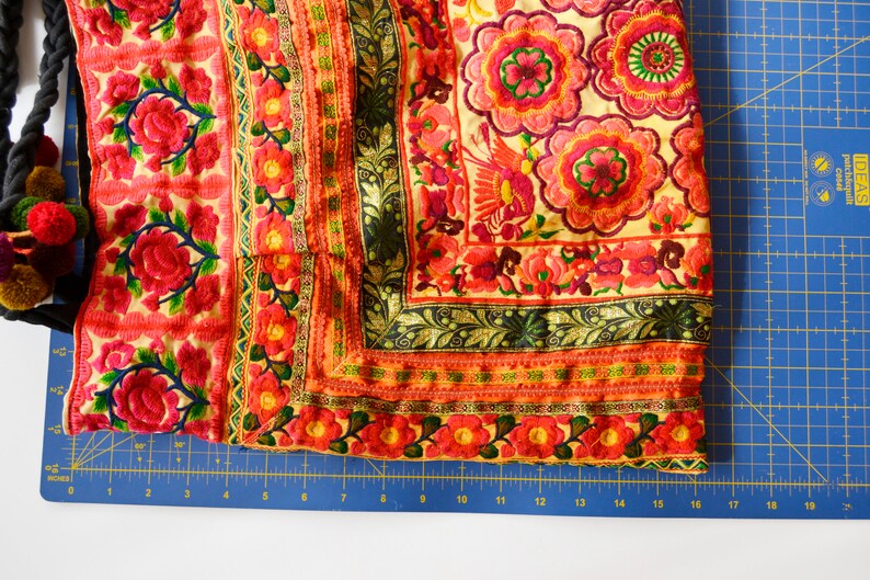 May include: A close-up of a colorful fabric with intricate embroidery featuring floral patterns and a bird design. The fabric is a mix of red, orange, yellow, green, and black.